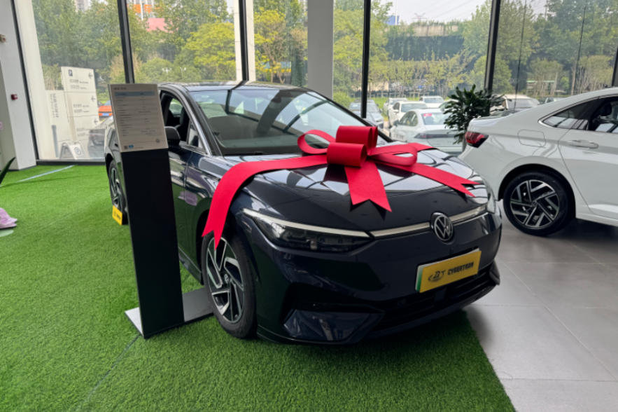 A dark blue Volkswagen electric sedan with a large red bow is showcased in a car showroom.