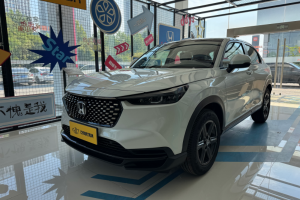 White Honda HR-V compact SUV in car showroom, front-side view with iconic grille, yellow license plate and alloy wheels.