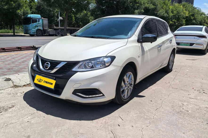 White Nissan Tiida compact hatchback three-quarter front view parked outdoors on concrete roadside with green trees backdrop