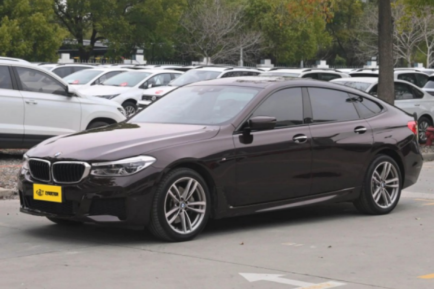 Black BMW 6 Series GT M Sport sedan in parking lot, side view with alloy wheels and tinted windows.
