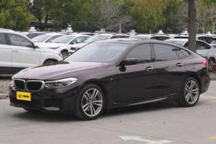 Black BMW 6 Series GT M Sport sedan in parking lot, side view with alloy wheels and tinted windows.