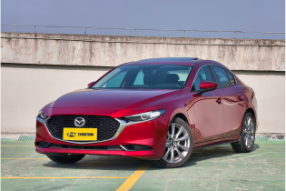 Soul red Mazda 3 sedan three-quarter front shot parked on rooftop parking lot under clear blue sky