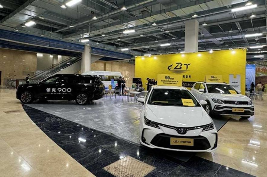 Auto show booth: black Lynk & Co 900, white Toyota, Volkswagen; yellow "ZBT" backdrop.