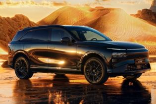 Sleek black electric SUV parked on a reflective wet surface, set against golden desert dunes at sunset.