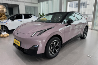 Light pink pure electric hatchback in indoor showroom, front-side view with futuristic LED lights, alloy wheels and yellow license plate.