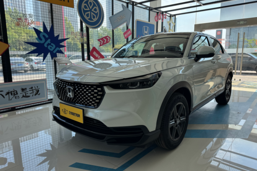 White Honda HR-V compact SUV in car showroom, front-side view with iconic grille, yellow license plate and alloy wheels.