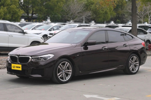 Black BMW 6 Series GT M Sport sedan in parking lot, side view with alloy wheels and tinted windows.